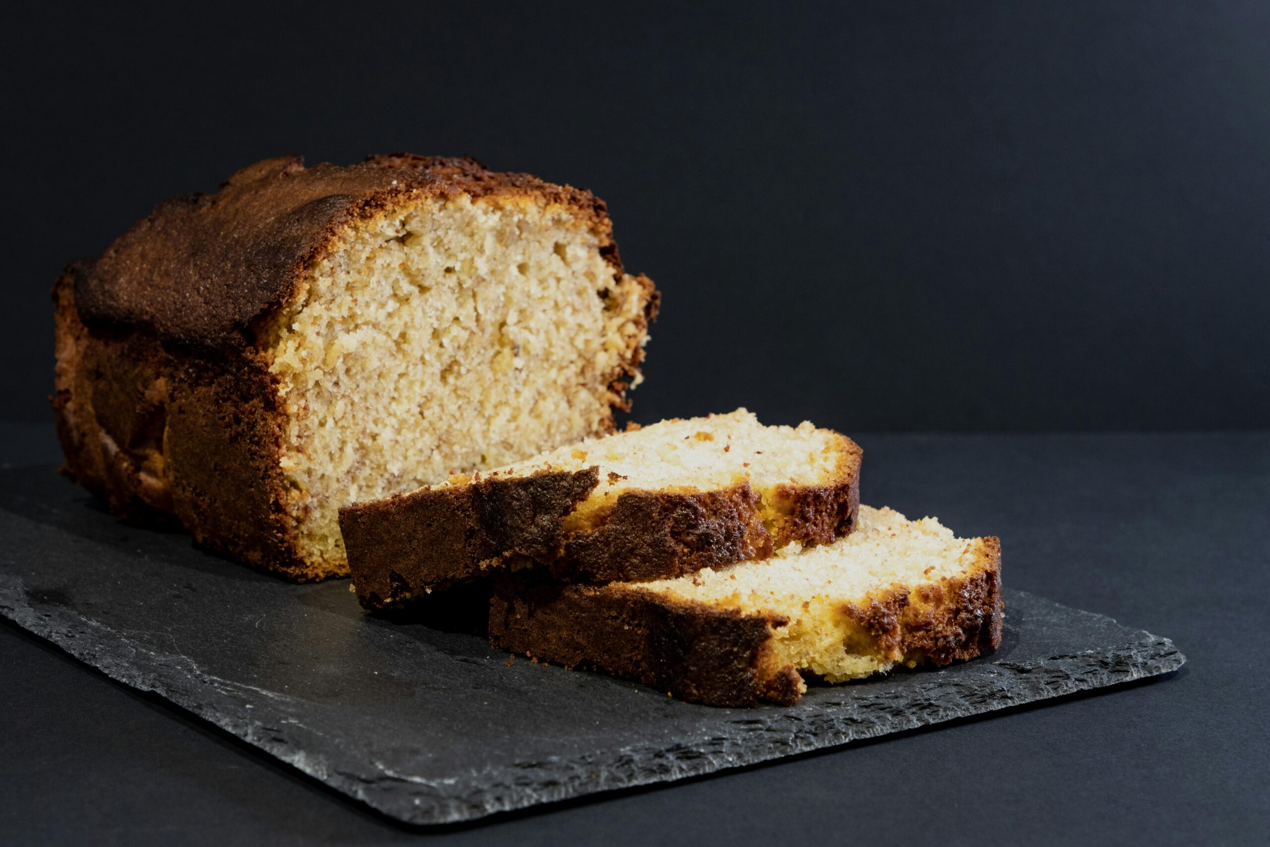 Tasty banana bread loaf with slices on a slate board, perfect for dessert or snack.