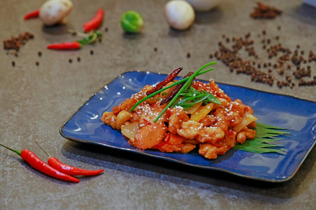 Close-up of a spicy chicken stir-fry dish garnished with chili peppers on a blue plate.