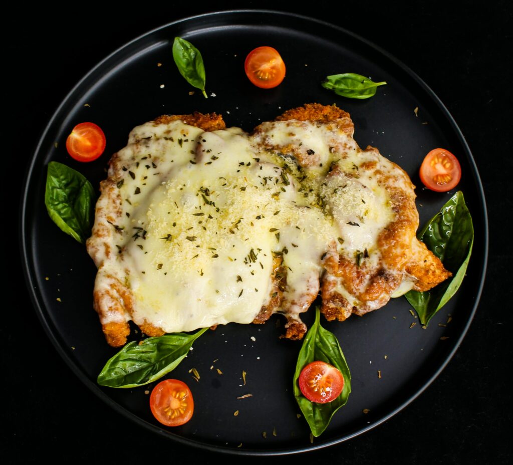 Delicious chicken parmesan topped with cheese, surrounded by cherry tomatoes and basil leaves.
