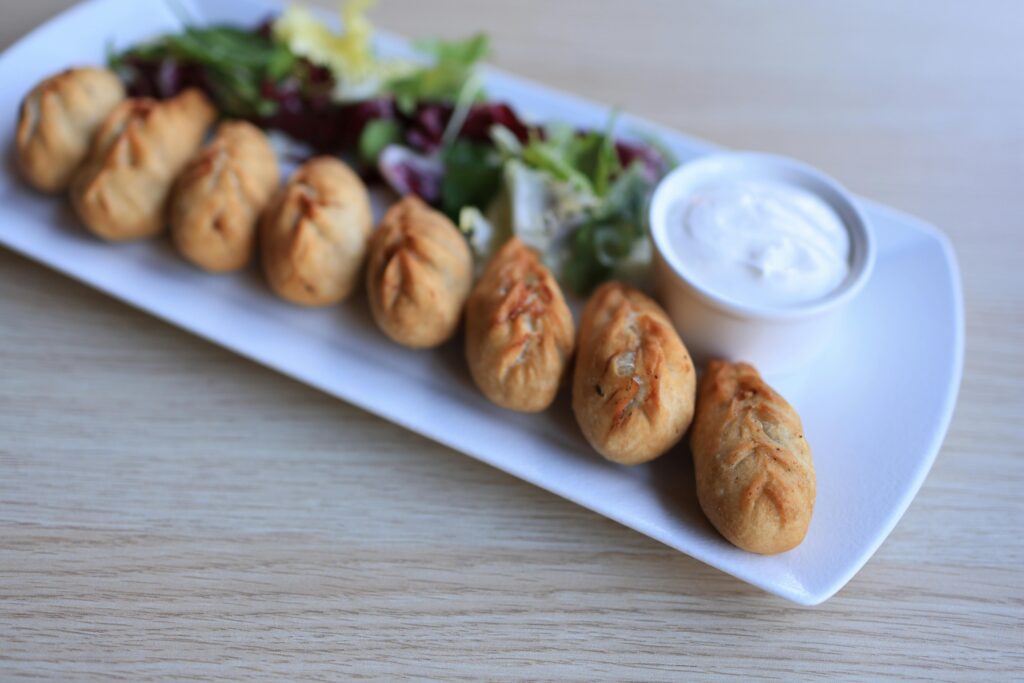 Close-up of savory dumplings with a fresh salad and creamy dip on a white plate.