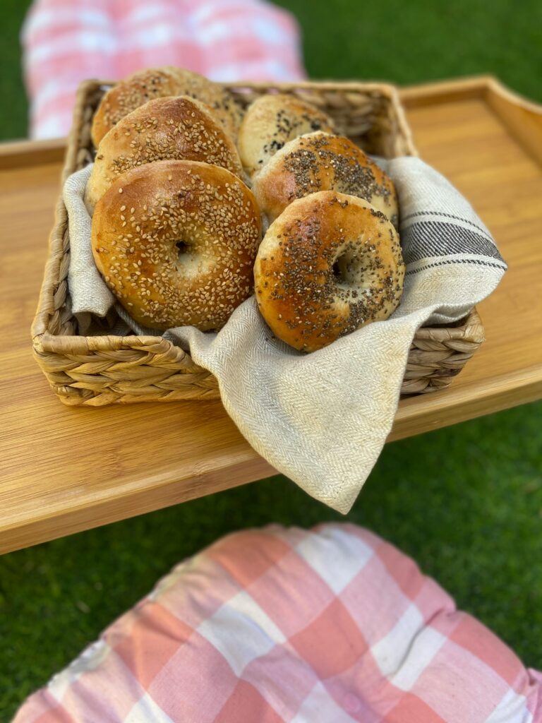 A basket of assorted fresh bagels on a wooden tray, perfect for a picnic.