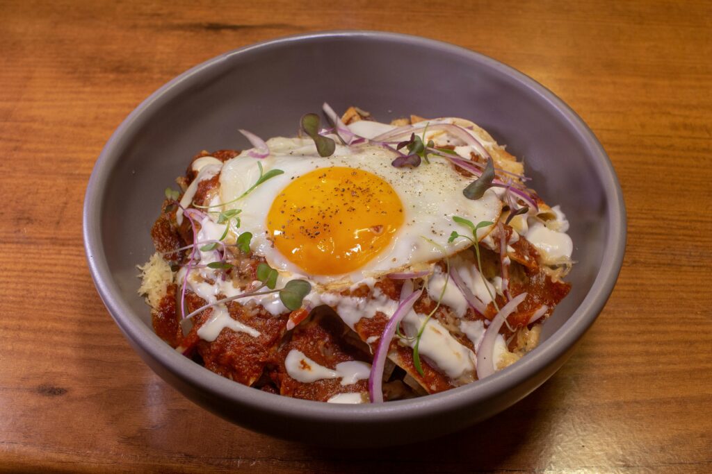 Appetizing bowl of chilaquiles topped with sunny-side-up egg, salsa, and microgreens.