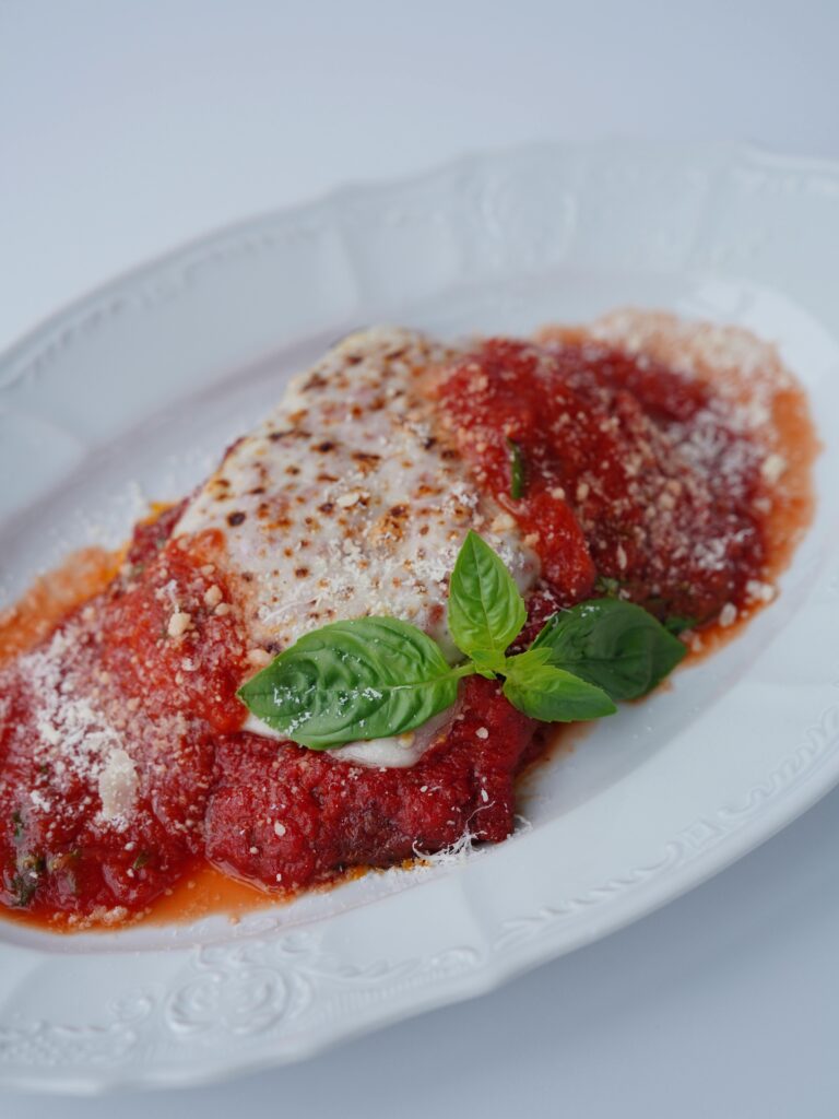 Close-up of a savory chicken parmesan dish topped with fresh basil leaves and served on a white plate.