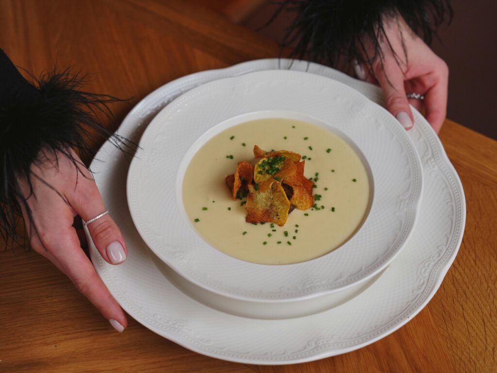 A gourmet creamy soup garnished with crispy toppings is beautifully served on white porcelain.