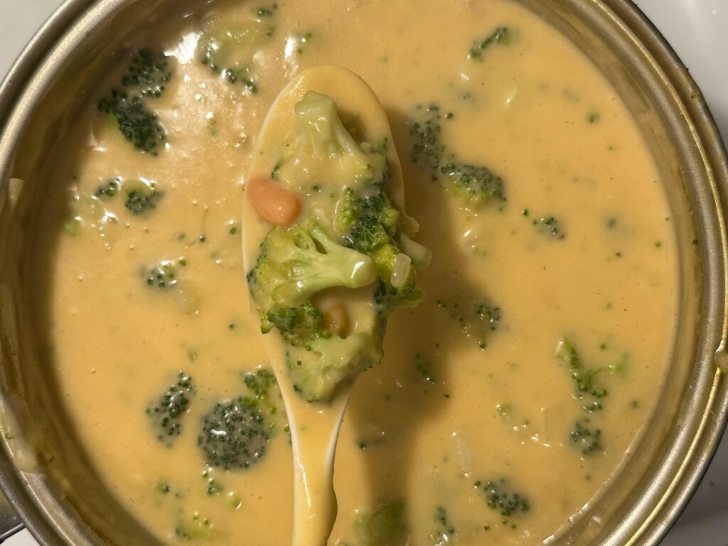 Creamy broccoli cheese soup in a pot with spoonful of vegetables. Perfect comfort food.