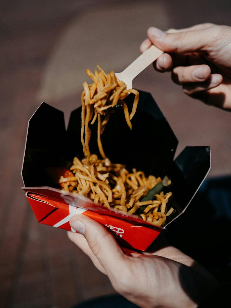 A detailed shot of fresh street food noodles in a takeaway box being held by hands.