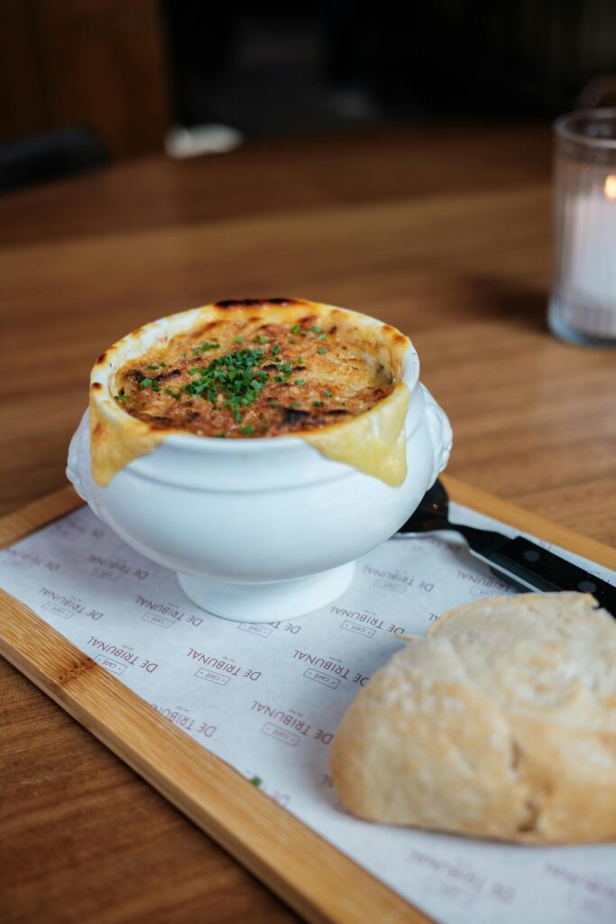 Close-up of French onion soup served in a white bowl with bread on a wooden table.