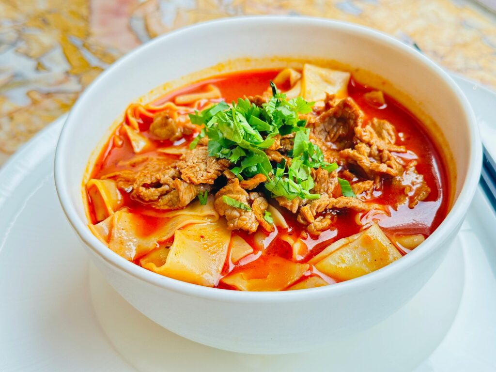 Delicious spicy lamb noodle soup garnished with cilantro in a white bowl. Perfect for hearty meals.