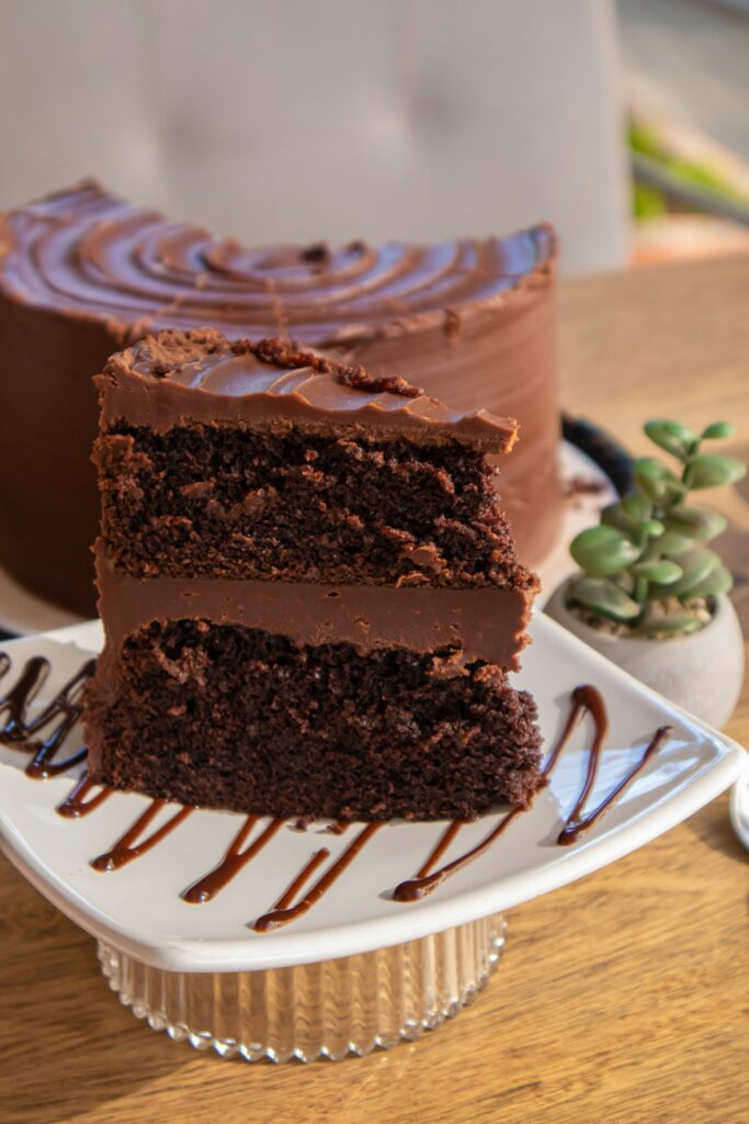Close-up of a decadent chocolate layer cake slice with frosting on a plate, perfect for dessert lovers.