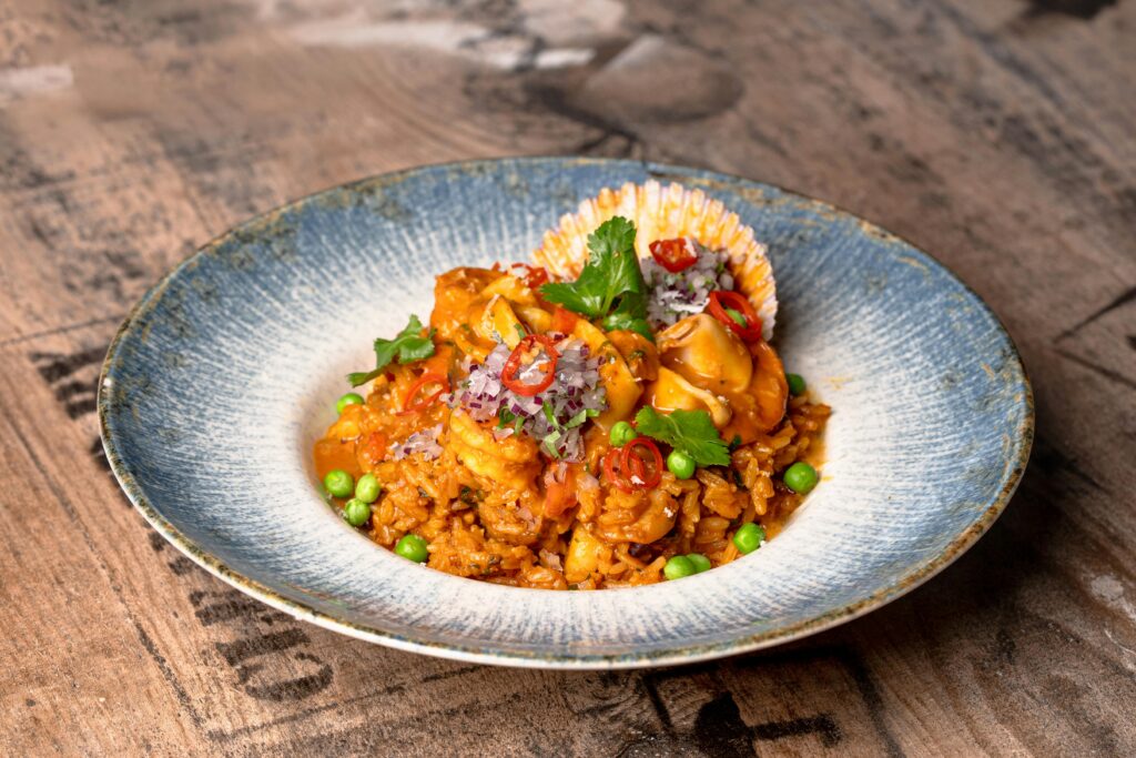 A vibrant seafood risotto garnished with fresh herbs and chili, served on a rustic wooden table.