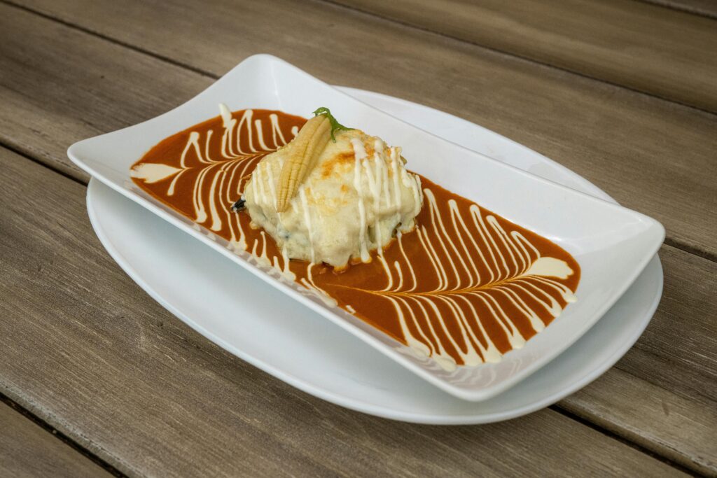 Delicious enchiladas plated with a vibrant red sauce and cream swirl, served on a wooden table.