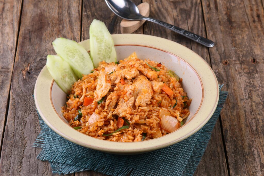 Savory chicken fried rice served with fresh cucumber slices on a rustic wooden table.