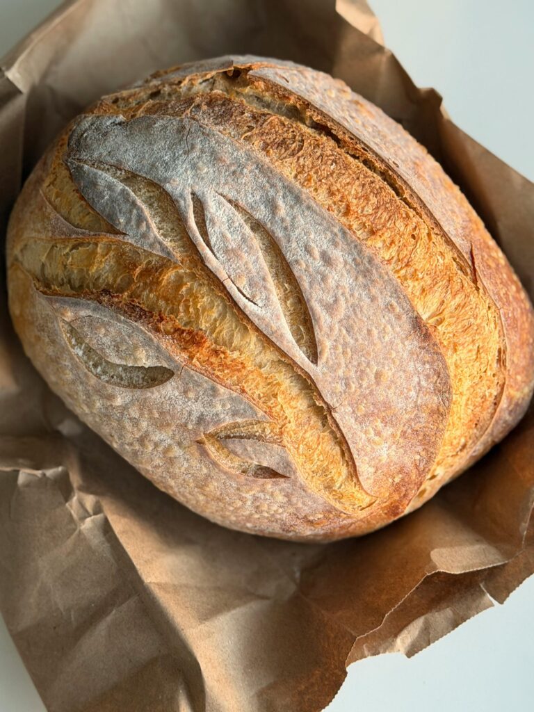 Freshly baked artisan sourdough loaf with a golden crust on paper.
