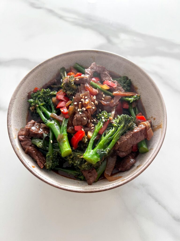 A flavorful beef and broccoli stir fry with red bell peppers in a bowl.