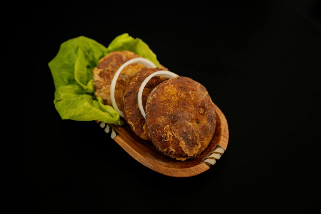 Three savory patties served with onions and lettuce on a wooden dish.