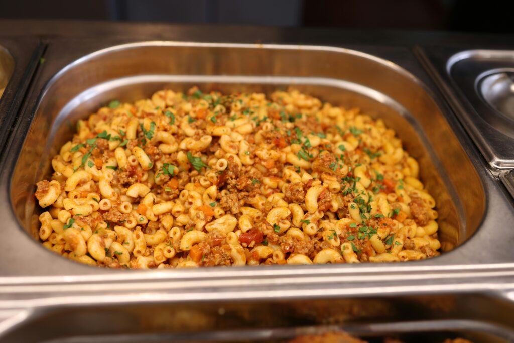 Close-up of a hot serving tray filled with macaroni and ground beef garnished with herbs.
