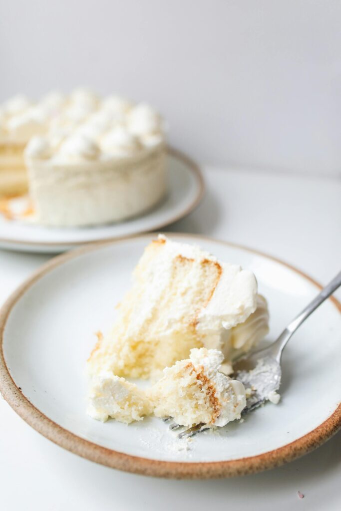Close-up of a delicious vanilla layer cake slice with frosting on a ceramic plate, perfect for foodies.