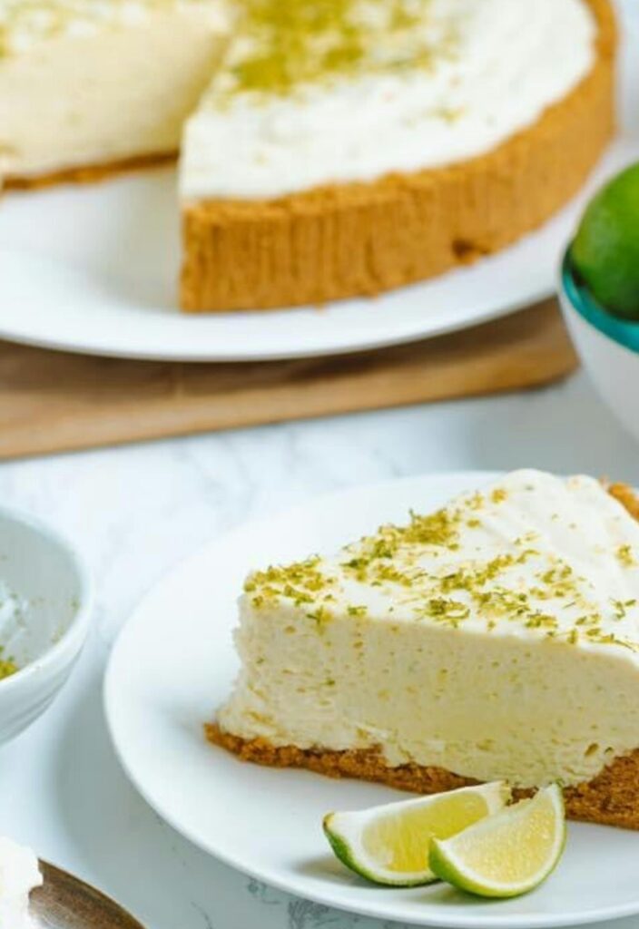 Delicious key lime pie slice on a white plate with limes on the side.