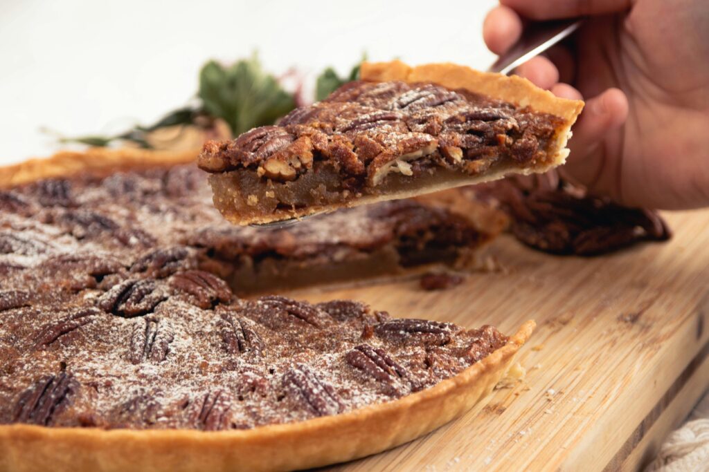 Close-up of a hand holding a sliced piece of homemade pecan pie with a sprinkle of powdered sugar.