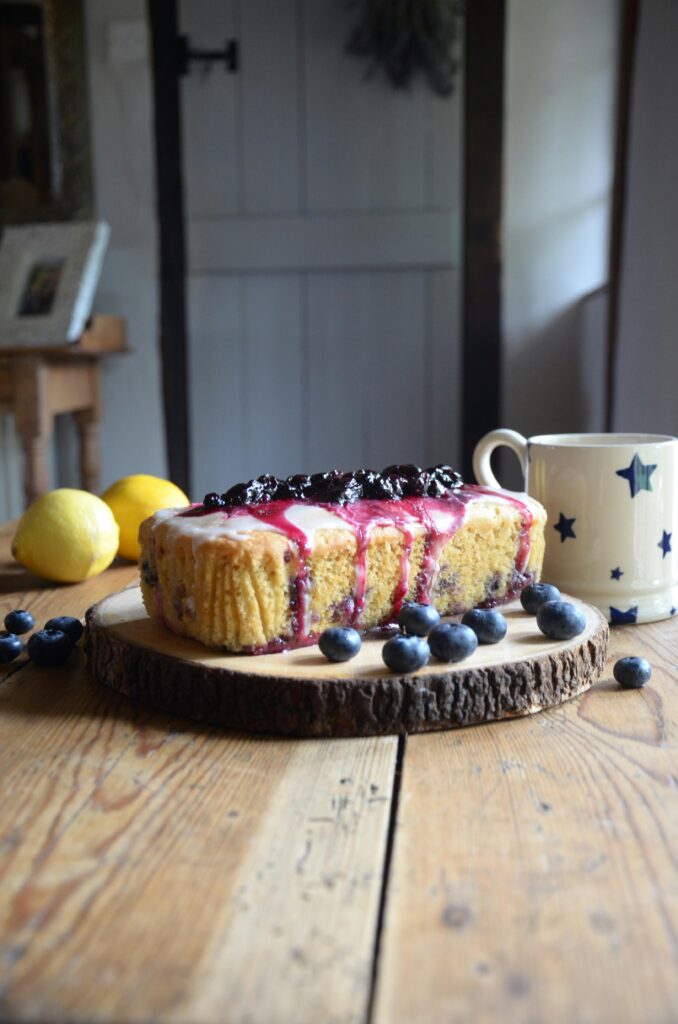 Homemade lemon blueberry cake with glaze on a rustic wooden board.