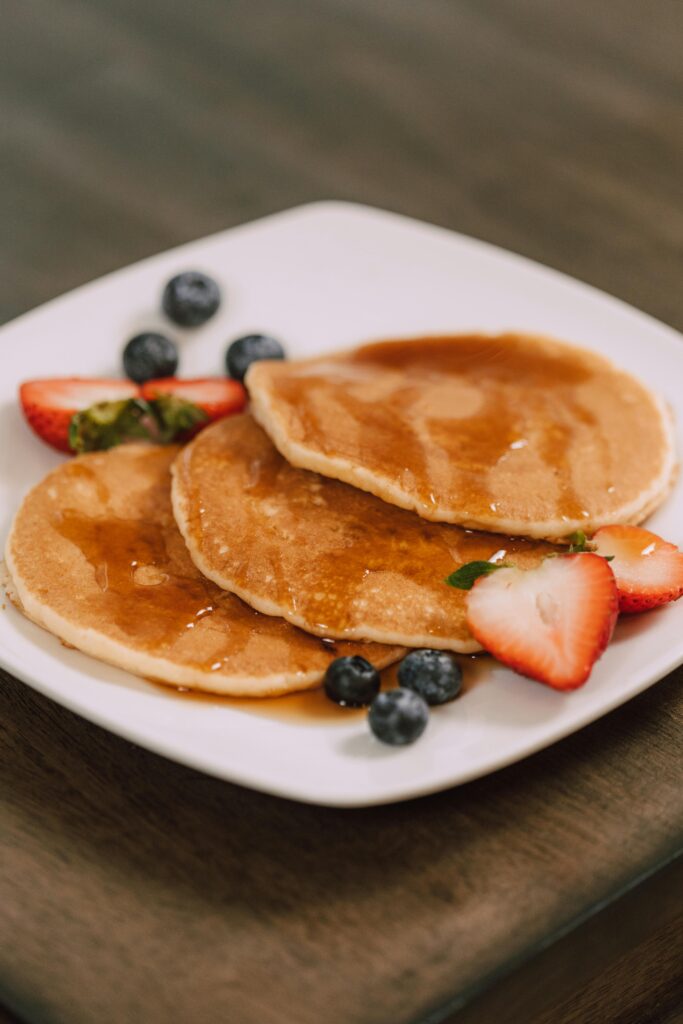 Mouth-watering pancakes served with fresh strawberries, blueberries, and syrup on a white plate.