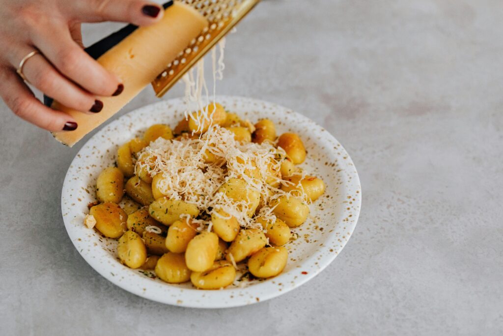 A ceramic plate of gnocchi with parmesan being grated by hand, highlighting Italian cuisine.