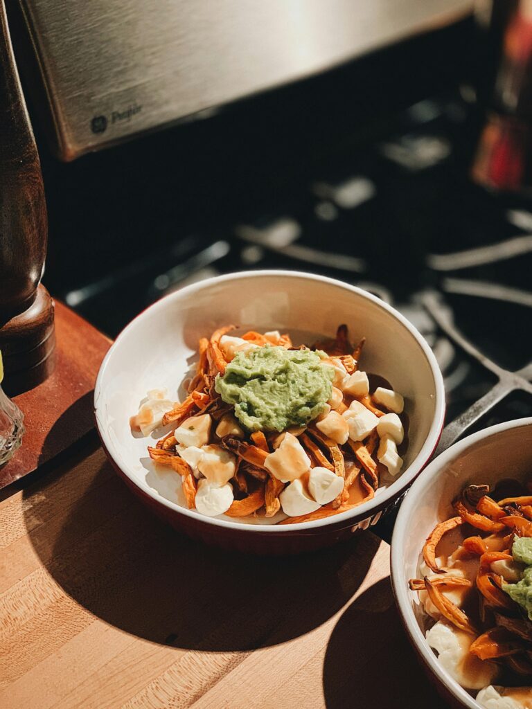 Delicious poutine with a twist, topped with creamy guacamole in a cozy kitchen setting.
