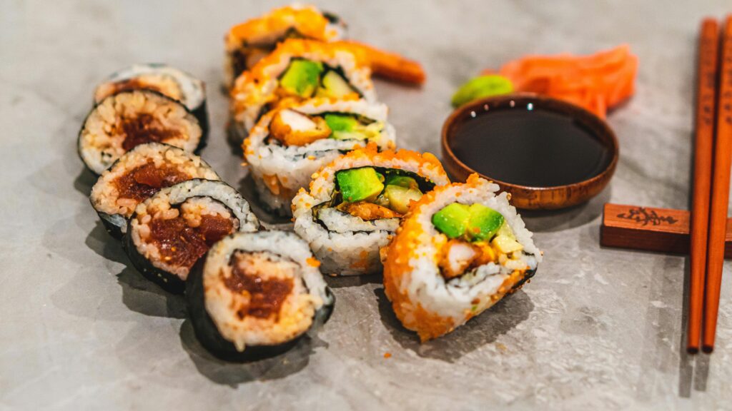 Close-up of assorted sushi rolls with soy sauce and chopsticks on a stone surface, showcasing fresh ingredients.