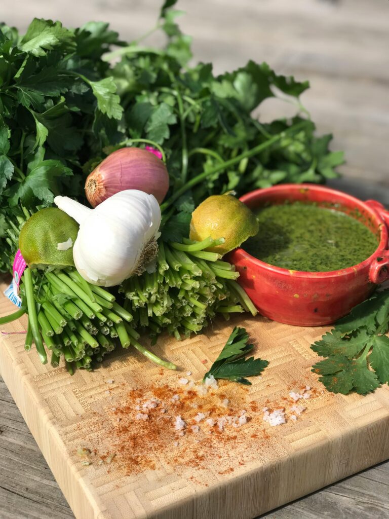 A vibrant collection of fresh herbs and ingredients including parsley, garlic, limes, and sauce displayed on a cutting board.