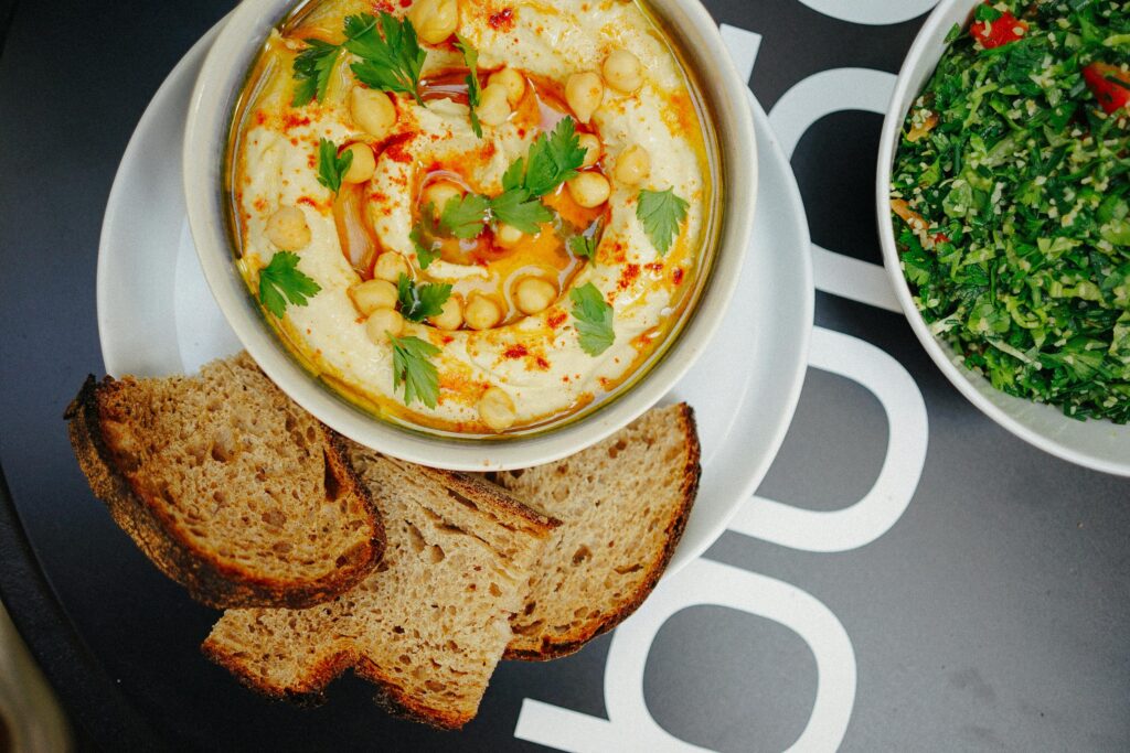 Top-view of homemade hummus garnished with parsley and served with bread slices, showcasing Mediterranean flavors.